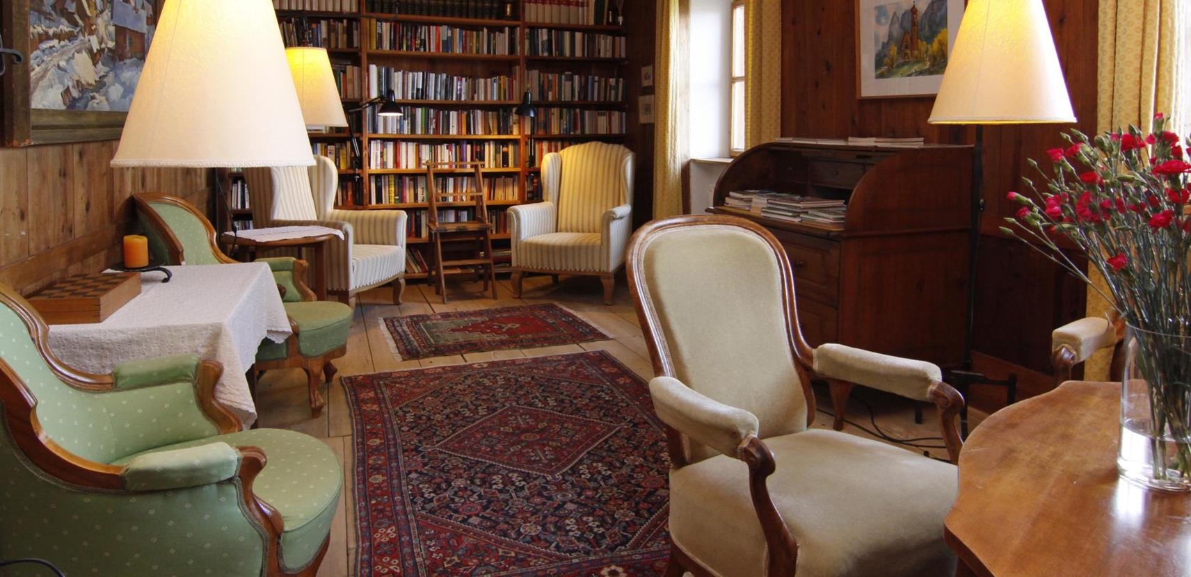 Unsere Bibliothek mit gemütlichen Sesseln, Teppichen und Bücherregalen bis zur Decke, umgeben von Holzvertäfelung und stimmungsvollem Licht.