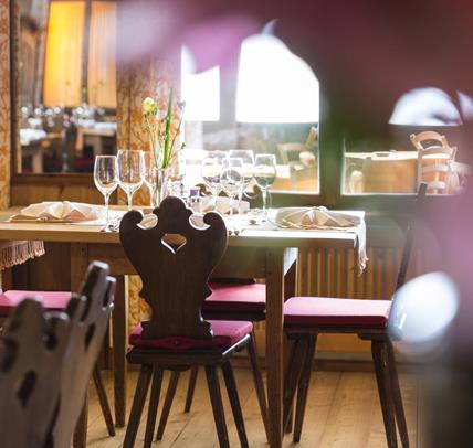 Stilvoll gedeckter Holztisch in unserem gemütlichen Speisesaal mit traditionellen Stühlen, weichen Sitzkissen und liebevollen Details, bereit für Gäste.