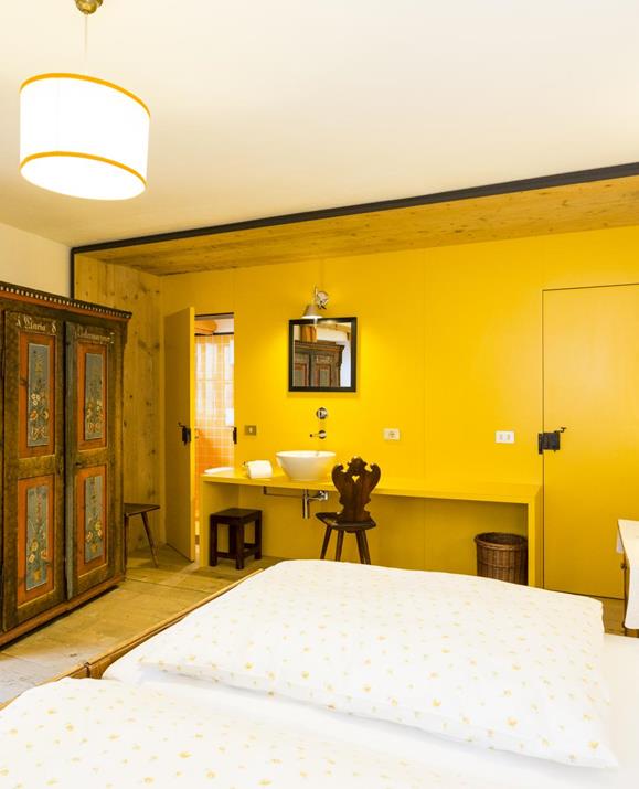 Camera doppia Pino senza rivestimenti in legno, ma con lavabo integrato, letto matrimoniale e un armadio antico decorato artisticamente.