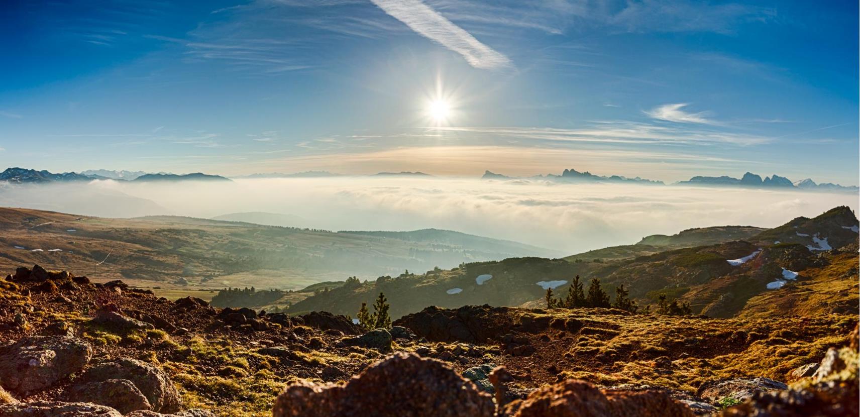 Sonnenaufgang über einer Alm mit einem atemberaubenden Panorama aus Nebelmeer, Dolomiten-Gipfeln und felsigem Vordergrund.