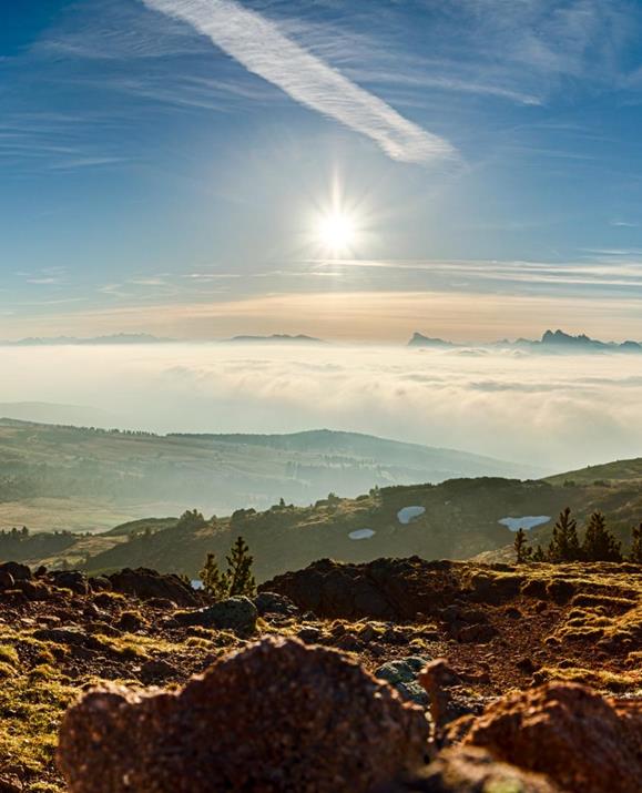 Sonnenaufgang über einer Alm mit einem atemberaubenden Panorama aus Nebelmeer, Dolomiten-Gipfeln und felsigem Vordergrund.
