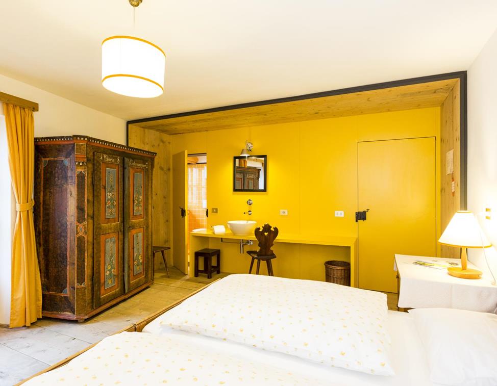 Double room Pine without wood paneling, featuring an integrated washbasin, a double bed, and an artistically painted antique wardrobe.