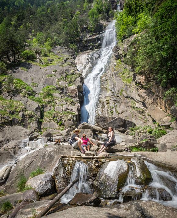 Eine Familie sitzt entspannt auf Felsen am Fuße eines imposanten Wasserfalls, umgeben von steilem Felsgestein und dichtem Wald inmitten der Südtiroler Berglandschaft.