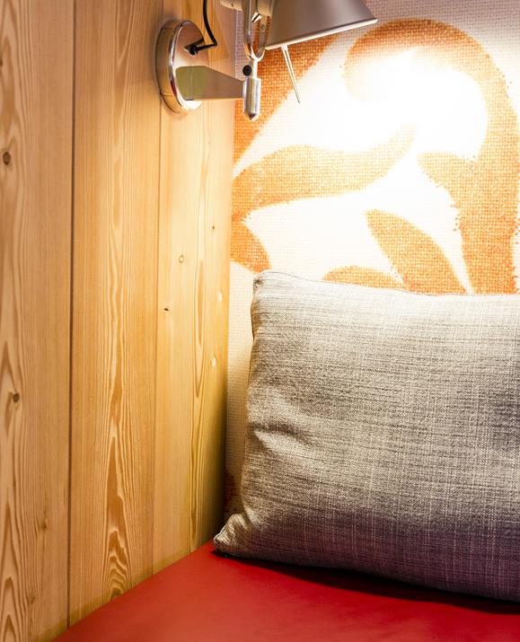 Nahaufnahme der Leseecke im Doppelzimmer Kirche: Man sieht eine eingeschaltete Leselampe und eine Ecke des Sofas mit einem Kissen.