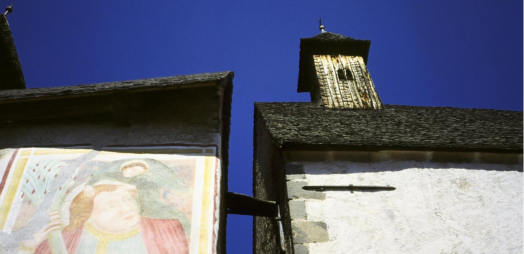 Detail of the facade of the Dreikirchen church with Gothic fresco and wooden bell tower set against a deep blue sky.