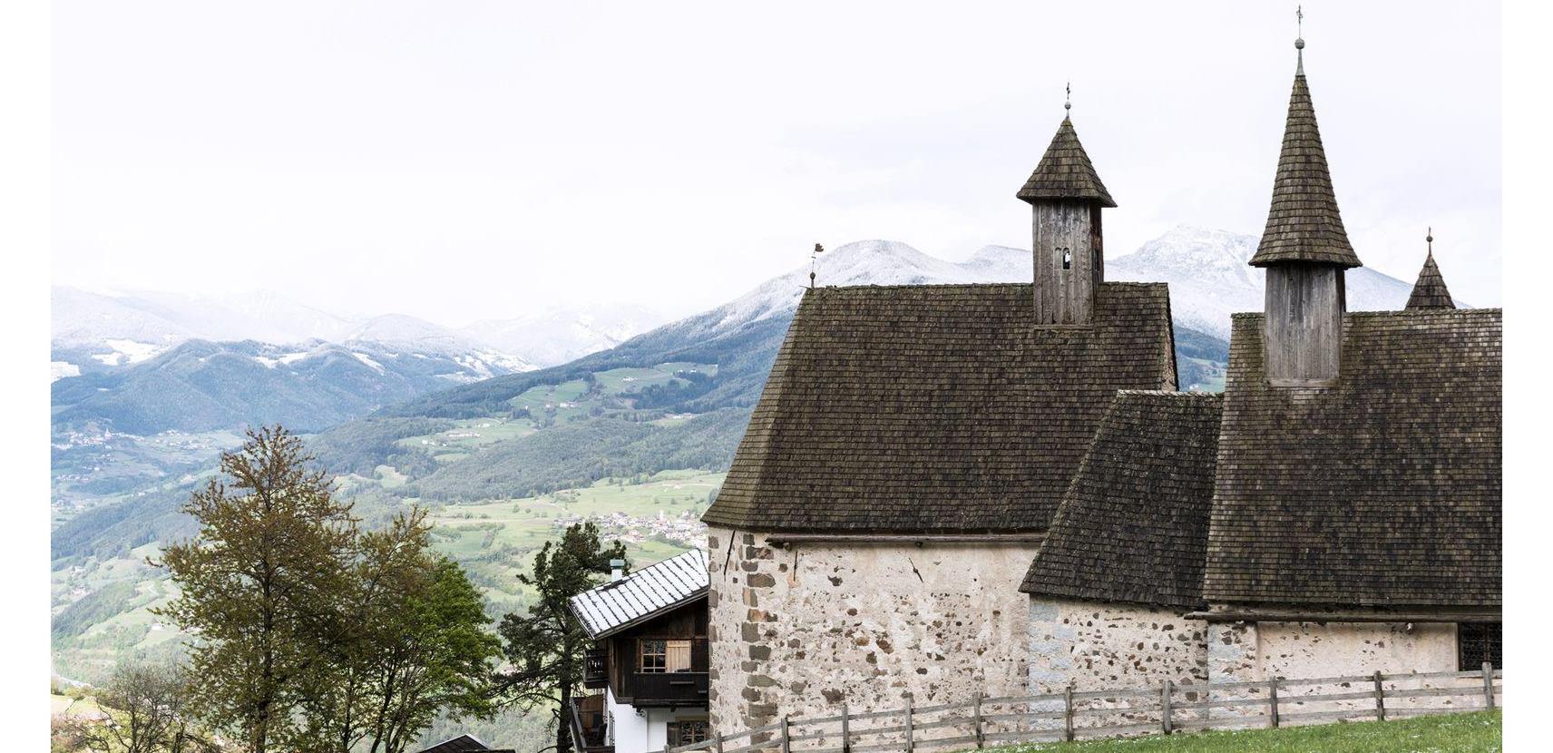View of the three churches of Dreikirchen with their distinctive shingle roofs and snow-covered mountains in the spring background.
